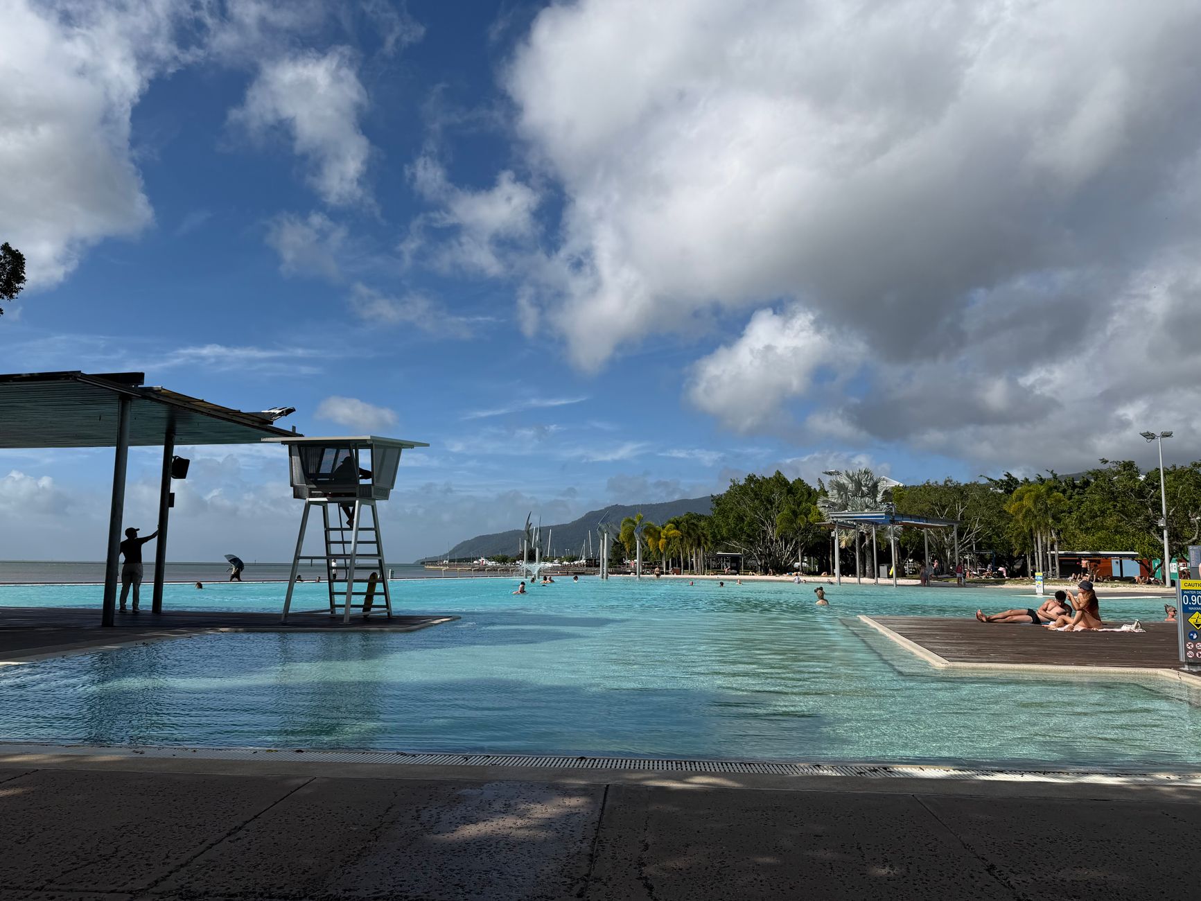 People swimming in the Cairns Esplanade Lagoon, a public waterfront pool, on a sunny day