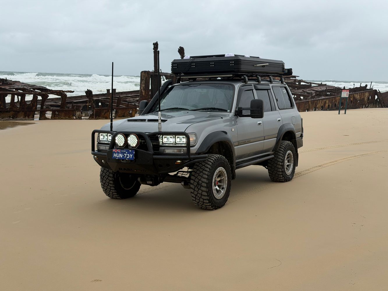 4x4 estacionado na areia de K'gari, ao lado dos destroços enferrujados do naufrágio SS Maheno