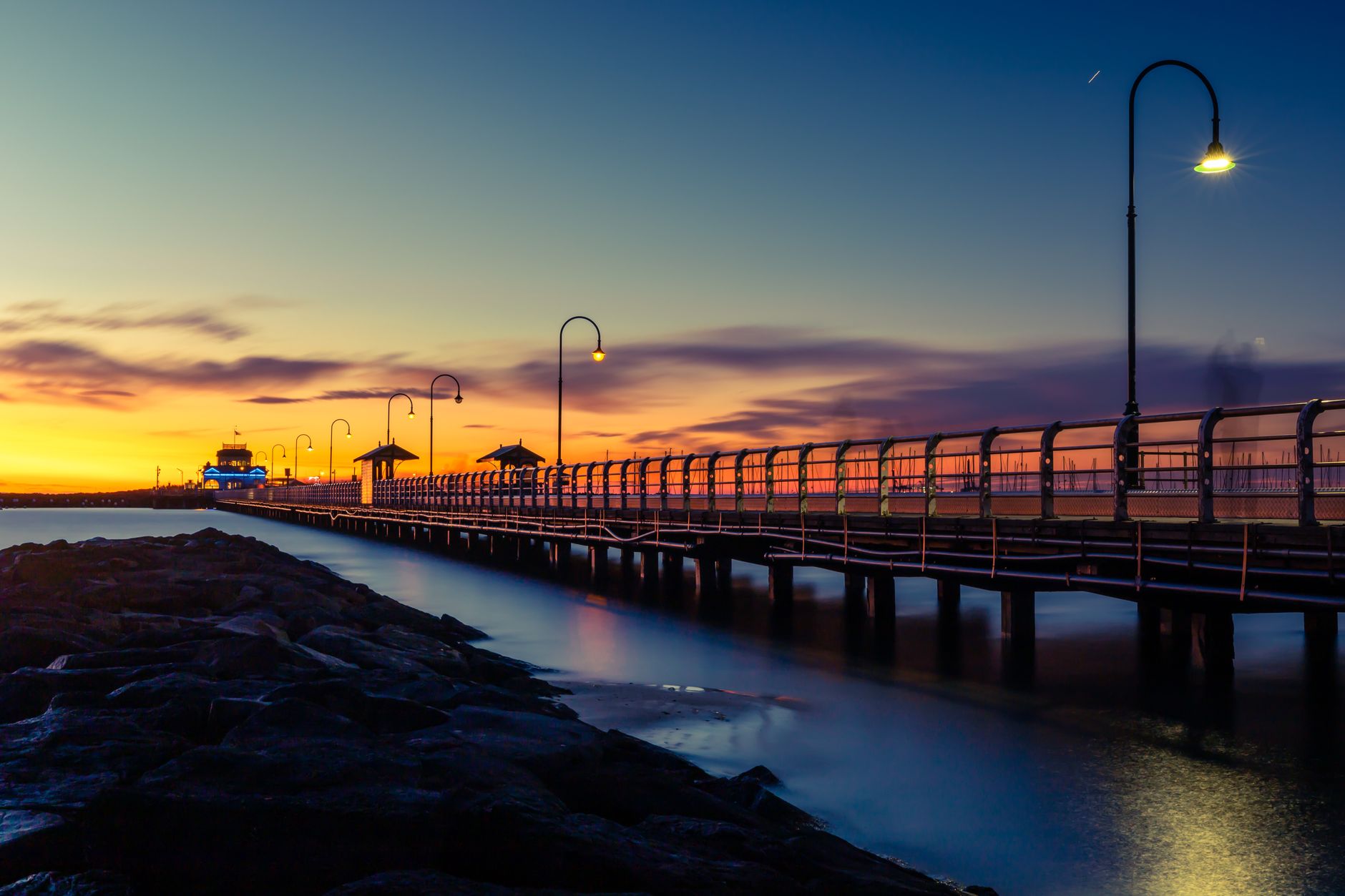 Muelle de St Kilda al atardecer, con cielo anaranjado y luces encendidas