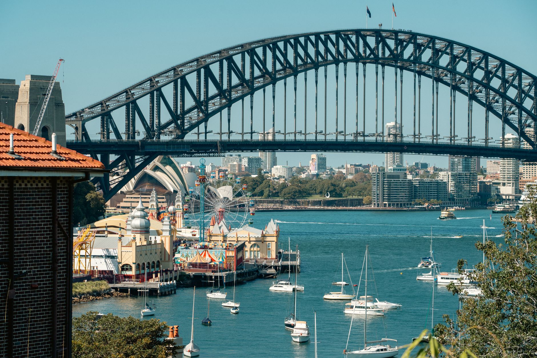 Sydney Harbour Bridge, Opera House y Luna Park vistos desde la bahía, con veleros en el agua