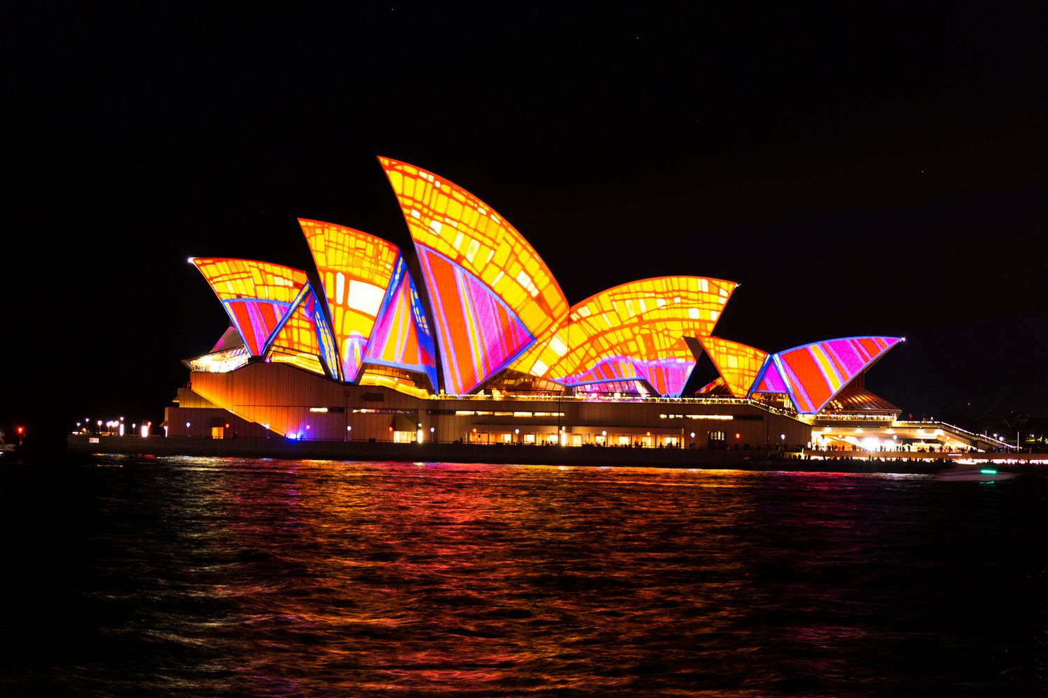Sydney Opera House with its sails lit up by light projections in orange and magenta tones during the Vivid Sydney festival