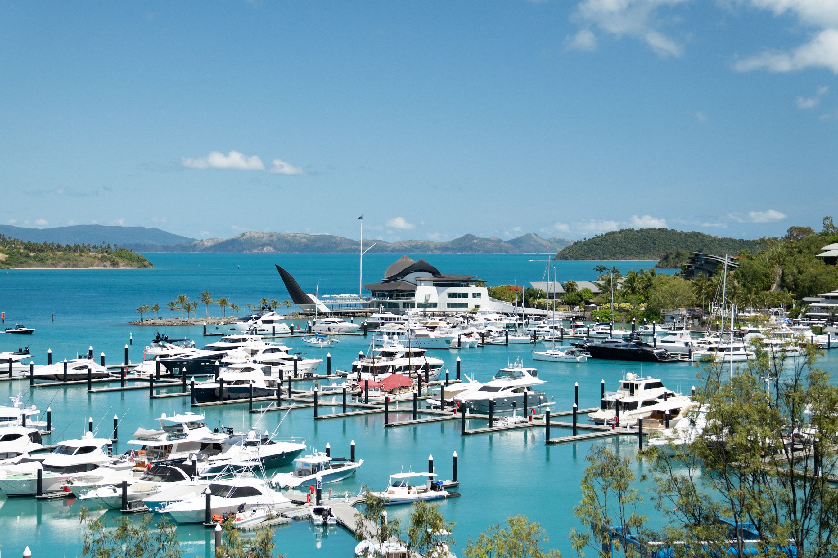 Aerial view of the Hamilton Island marina, with yachts and boats anchored and the Whitsunday islands in the background