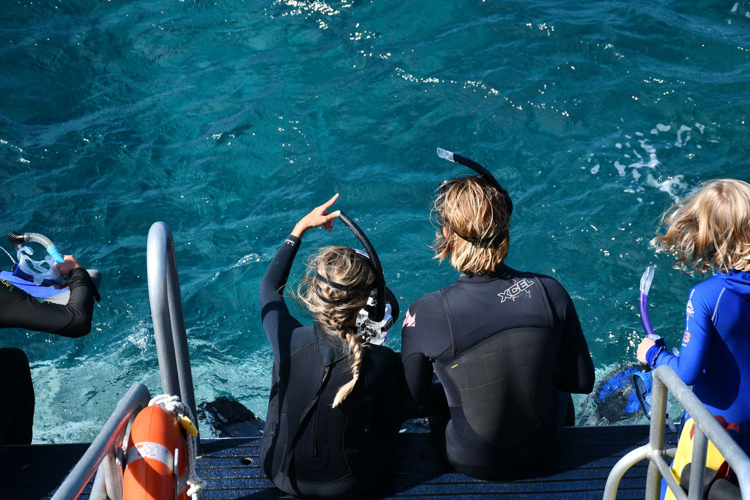 Group getting ready to snorkel, sitting on a boat platform over clear blue water